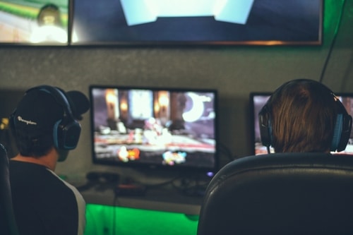 Two guys facing monitors playing video games